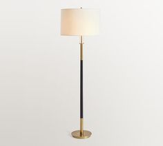 a floor lamp with a white shade on the top and a black pole underneath it