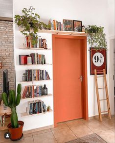 an orange door in a white room with bookshelves and plants on the shelves