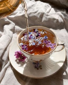 tea being poured into a cup with purple flowers on the saucer next to it