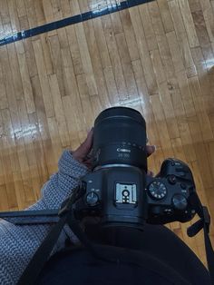 a person holding a camera up to their face on a wooden floor in front of a basketball court