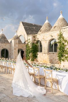 a woman in a wedding dress standing next to a table with white clothed tables and chairs