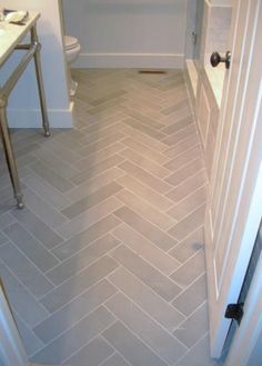 a bathroom with white walls and grey herringbone tile