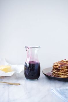 a plate topped with pancakes covered in blueberry sauce next to a glass pitcher filled with syrup