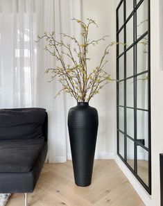 a black vase with flowers in it sitting on a wooden floor next to a couch