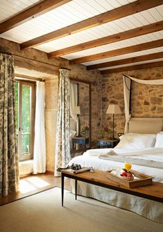 a bed sitting in a bedroom next to a window covered in white sheets and pillows