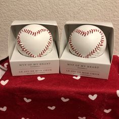 two white baseballs with red stitching in a box on a tablecloth covered surface