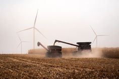 a tractor is driving in the middle of a field with wind turbines behind it on a foggy day