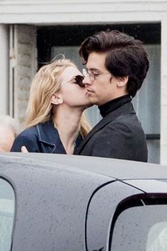 a man and woman kissing in front of a car