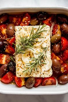 a square white dish filled with olives, tomatoes and fish