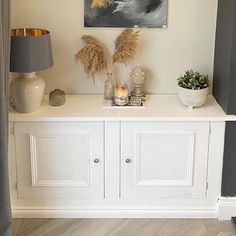 a painting is hanging on the wall above a white cabinet with two vases and plants