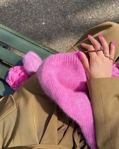 a woman wearing a pink hat and coat with her hands in the air while sitting on a bench