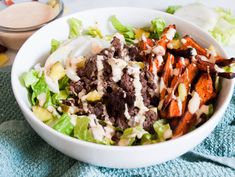 a white bowl filled with lettuce, carrots and other food on top of a blue towel