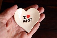 a hand holding a ceramic heart with the word i love my cat written on it