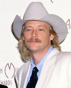 a man in a white suit and tie with a mustache wearing a cowboy's hat