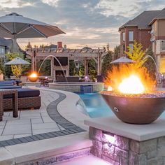 an outdoor fire pit in the middle of a patio with lounge chairs and umbrellas