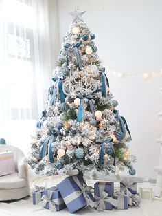 a white christmas tree with blue and silver ornaments on it's branches, surrounded by presents