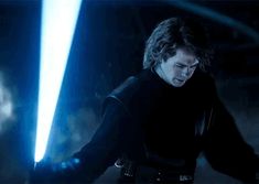 a man holding a light saber in his right hand and wearing a black shirt with blue lights behind him