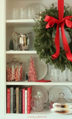 a christmas wreath on top of a white book shelf filled with books and other holiday decorations