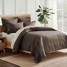 a bed with brown linens and pillows in a white room next to a potted plant