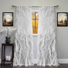 a window with white ruffled curtains in front of it and pictures on the wall