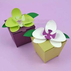 two paper flowers sitting on top of a purple box with one flower in it's center