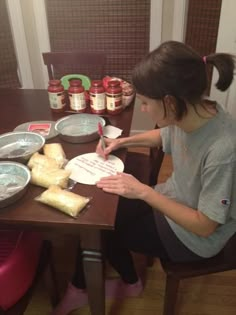 a woman sitting at a table writing on a piece of paper with jams in the background