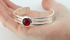 A charming and easy to wear open adjustable/expandable cabochon bangle. The metal component of the bangle is shiny, superior silver plated copper, with the focal point being a vintage Swarovski Ruby crystal cabochon. Ruby is the traditional birthstone for the month of July and celebrates 40 years of marriage, therefore making an ideal gift.  The colour of ruby is an attractive, vibrant shade of red. The cabochon set within the bangle is vintage, dating back to the 1970's.  DIMENSIONS The bangle is made from superior silver plated copper. Copper is a malleable metal, therefore size adjustment can be carried out. The bangle is open and will fit wrist sizes from 15cm (6 inch) to 20cm (8 inch). Size adjustment is achieved by either squeezing the ends inwardly together to make smaller or by exp 40 Years Of Marriage, Cabochon Ruby, Month Of July, Shade Of Red, Gemstone Bangle, Ruby Crystal, July Birthstone, Cuff Bangles