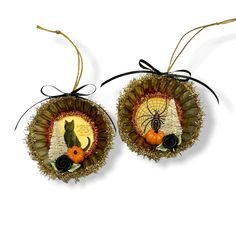 two ornaments made out of straw with cats and pumpkins on them, hanging from twine strings