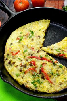 an omelet is shown in a skillet on a green surface with tomatoes