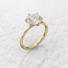 a yellow gold engagement ring with a single diamond in the center on a white surface