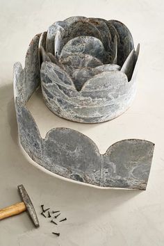 an old metal flower pot sitting on top of a white table next to a hammer