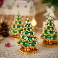 three small christmas trees are sitting on a table with other ornaments around them and one is gold