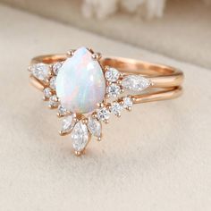 a white opal and diamond ring sitting on top of a cushioned surface,