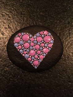 a rock with pink and blue dots in the shape of a heart on black background