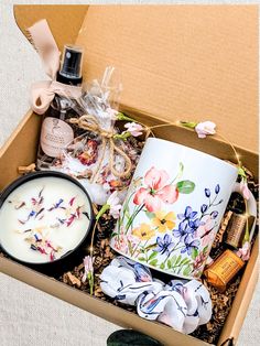 an open box containing a candle, coffee mug and various other decorative items with flowers on them