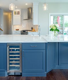 a kitchen with an island and wine cooler in the center, surrounded by blue cabinets