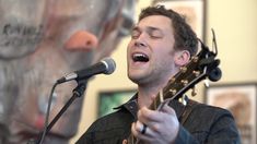 a man singing into a microphone while holding an acoustic guitar in front of his face