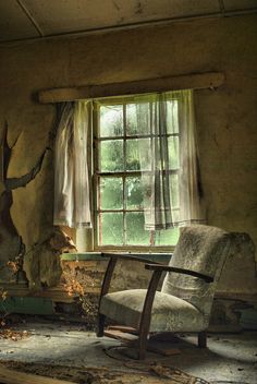 an old chair sitting in front of a window next to a broken up tree trunk