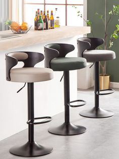 three modern bar stools in front of a kitchen counter with bottles on the back