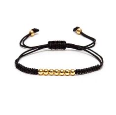 the black cord bracelet with gold beads is shown in front of a white background, and has