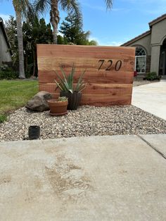 a wooden sign sitting on top of a gravel covered ground next to a planter