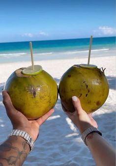 two people holding up coconuts on the beach