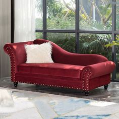 a red couch sitting in front of a window with a white pillow on top of it