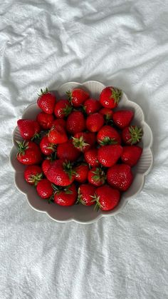 a white bowl filled with lots of ripe strawberries on top of a white sheet