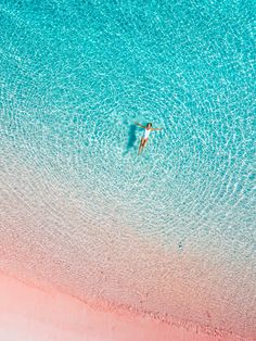 an aerial view of a person swimming in the blue water on a pink sand beach