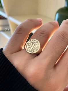 a person's hand wearing a gold ring with an emblem on the middle finger