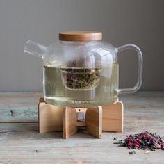 a glass tea pot filled with green tea sitting on top of a wooden stand