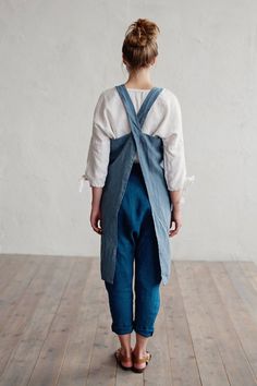 a woman in overalls is standing on a wooden floor with her back to the camera