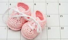 two pink crocheted baby shoes sitting on top of a calendar