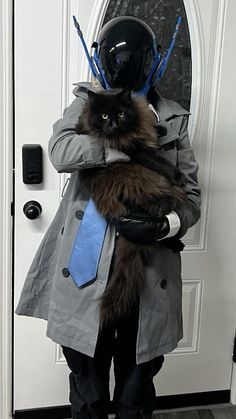 a person wearing a suit and tie holding a cat in their arms while standing next to a door